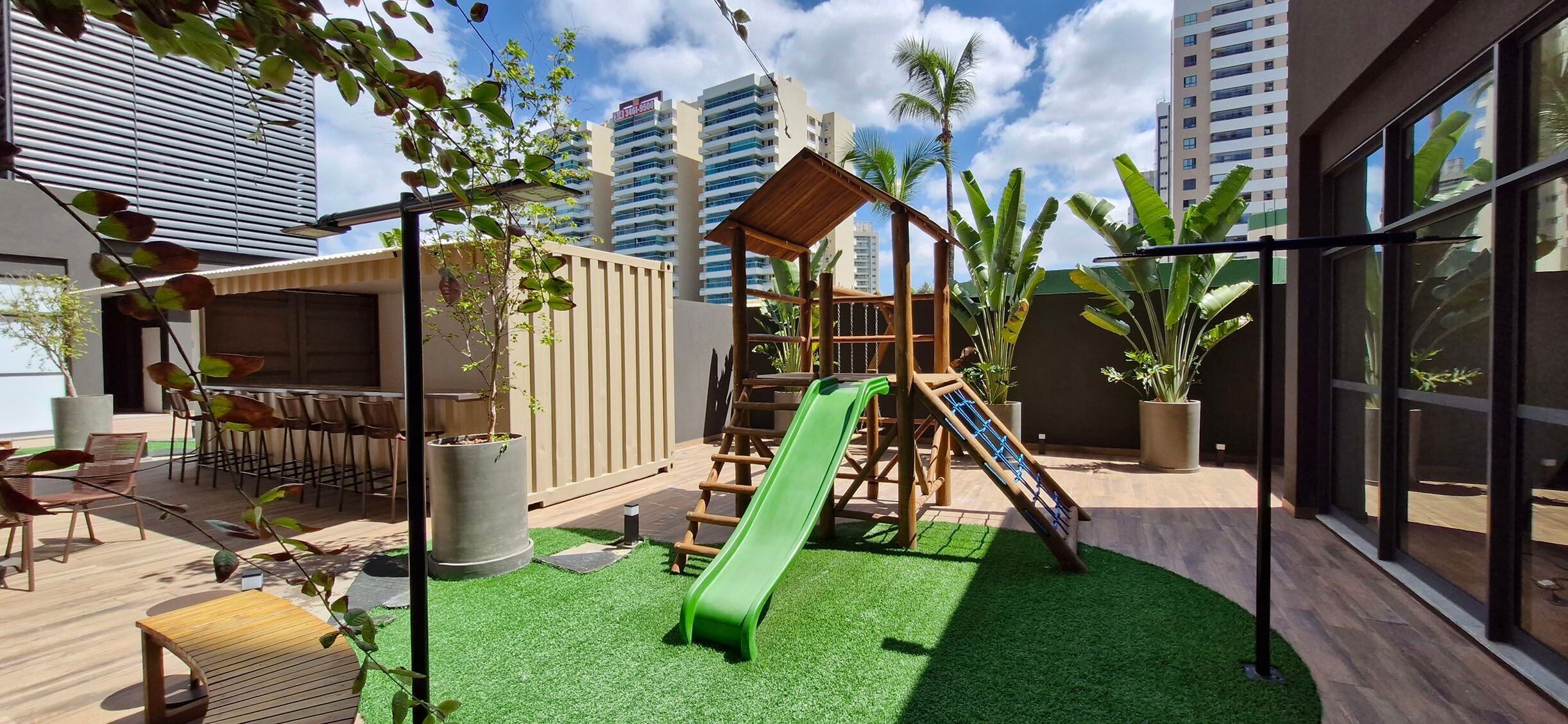 An outdoor patio with a children's play area, including a slide and climbing structure, surrounded by potted plants and seating.