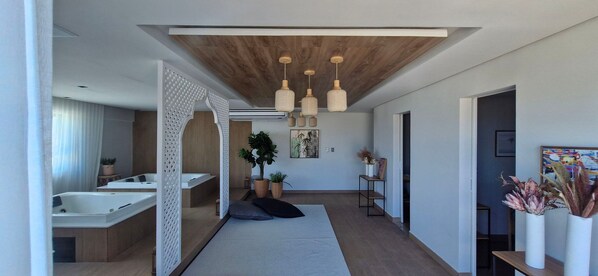 Interior moderno com teto de madeira, luminárias pendentes, banheira, sofá e plantas em vasos.