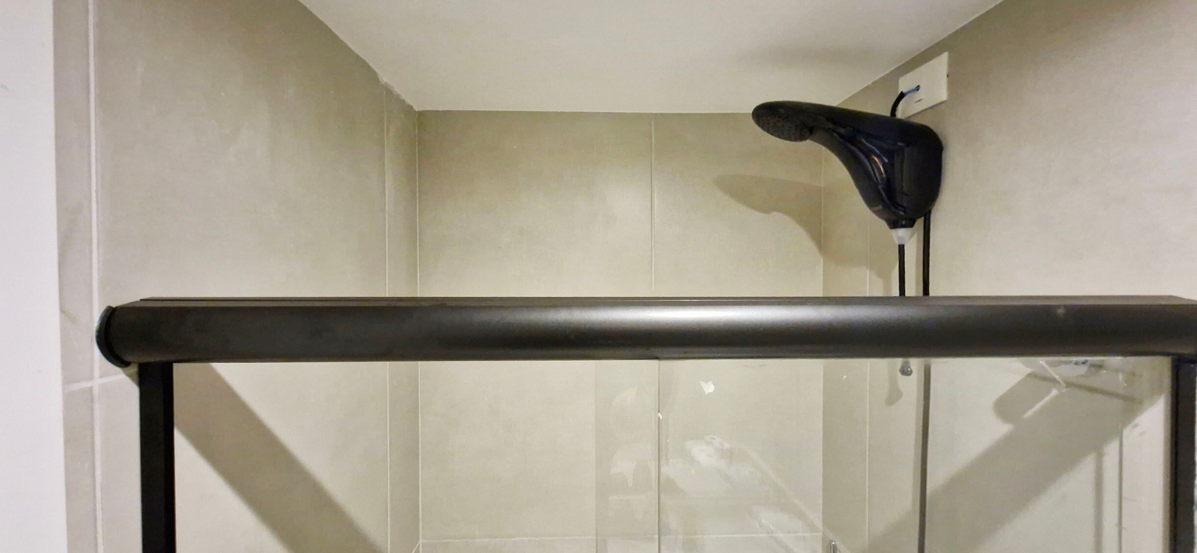 A bathroom with a shower area, a black towel rack, and a mirror.