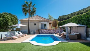Un giardino con piscina, lettini prendisole, un'area salotto coperta e un muro in pietra.