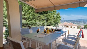 Una terrazza esterna con tavolo apparecchiato per mangiare, circondata da sedie e vista su un paesaggio montano.