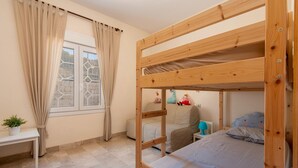 Una camera con un letto a castello, una finestra, tende, un tavolino e una pianta.