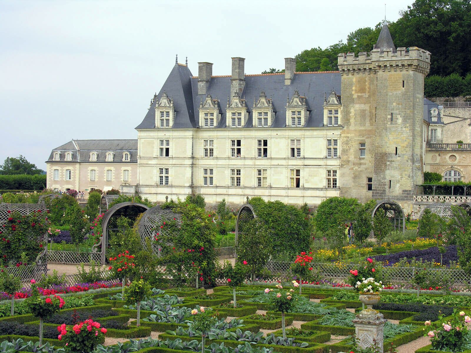 Il s’agit d’un grand bâtiment historique doté de nombreuses fenêtres et d’une tour. Devant, on trouve un jardin bien entretenu, où poussent diverses plantes et fleurs.