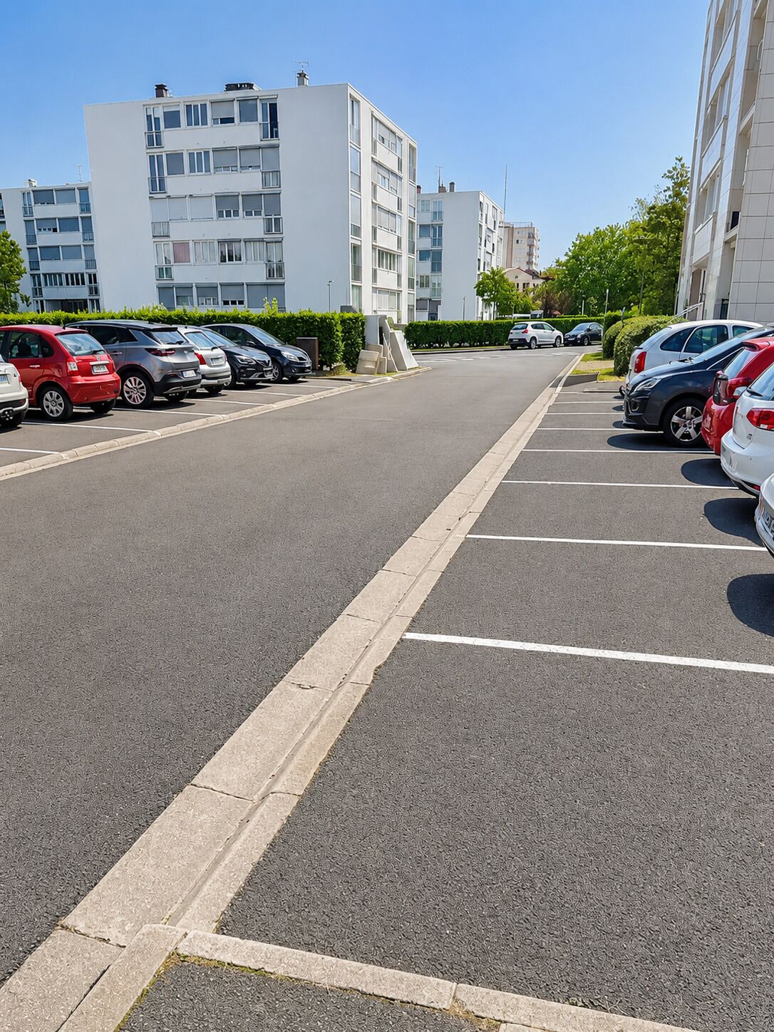 Un estacionamiento con varios autos, cielo despejado y edificios modernos al fondo.