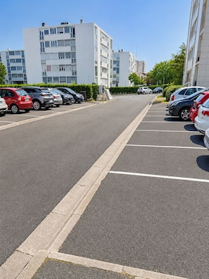 Un parking rempli de voitures, un ciel dégagé et des bâtiments modernes en arrière-plan.