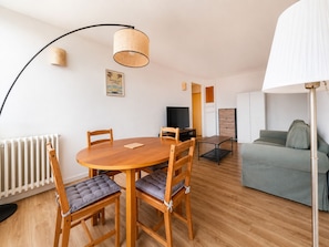 Un salon moderne avec une table de salle à manger ronde en bois, deux chaises, un canapé, un téléviseur et un lampadaire.