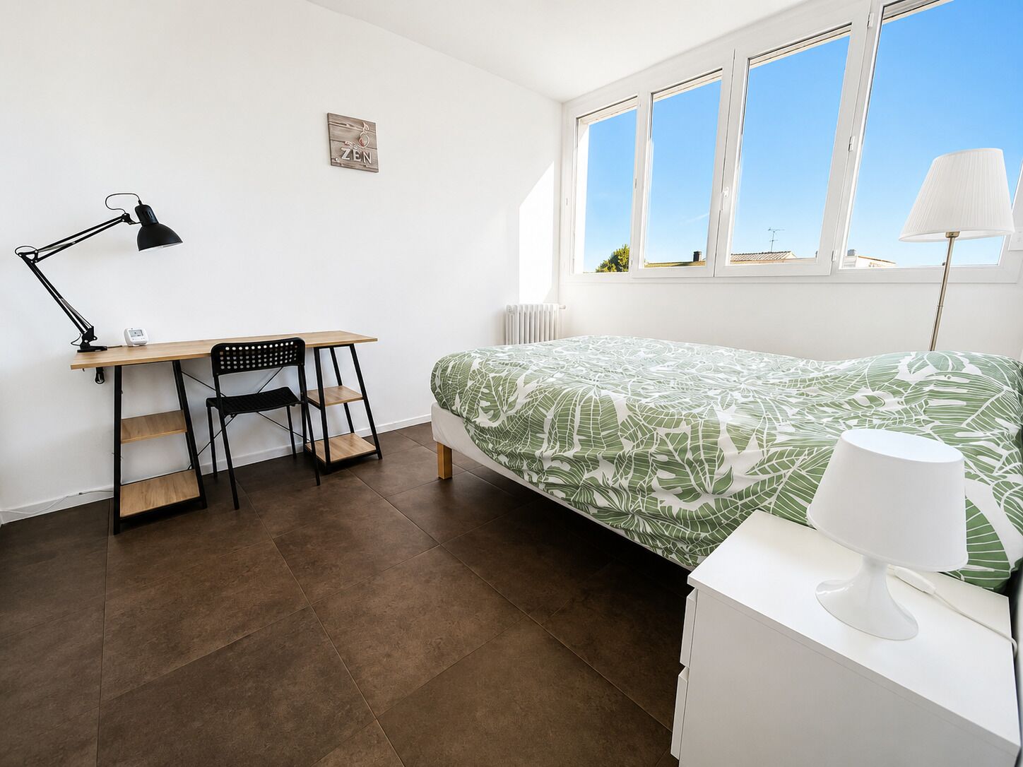 Un dormitorio con cama, escritorio, silla, lámpara y ventana.