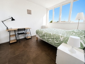 Une chambre à coucher avec un lit, un bureau, une chaise, une lampe et une fenêtre.