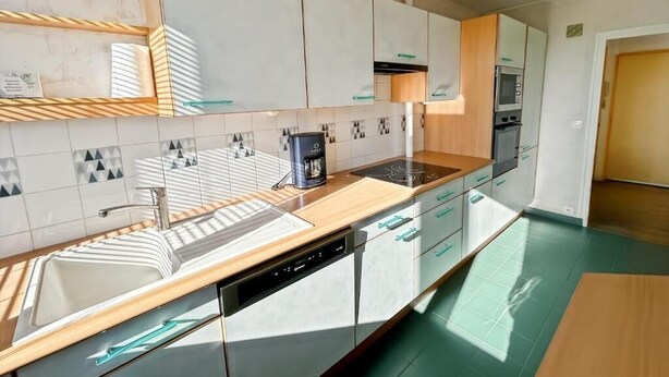 A modern kitchen with white cabinets, a built-in dishwasher, a coffee maker, and a microwave. - Spacious 3-bedroom apartment in Tours Nord near the tramway (Tours)