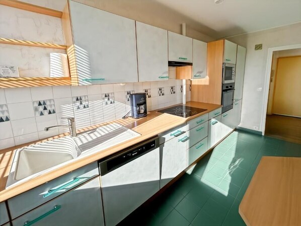 A modern kitchen with white cabinets, a built-in dishwasher, a coffee maker, and a microwave. - Spacious 3-bedroom apartment in Tours Nord near the tramway (Tours)