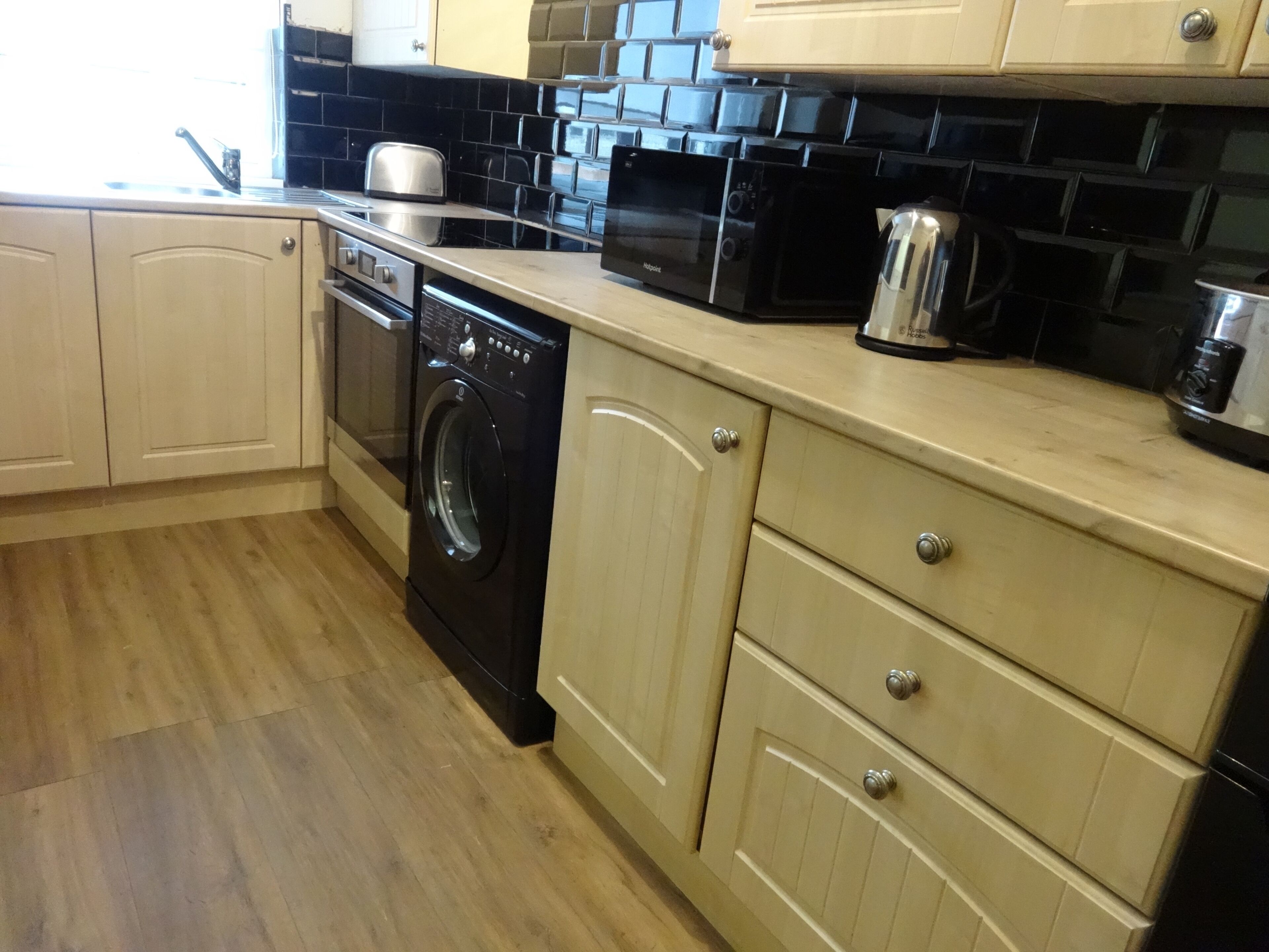 A kitchen with a washing machine, microwave, and toaster.