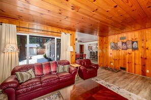 A wooden-paneled room with a leather sofa, a dining table, and a view through a glass door. - Al Tahoe Cabin-Vintage Meets Modern 3 Bed, 2 B (South Lake Tahoe)