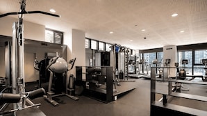 Et moderne fitnesscenter med forskellig træningsudstyr, store vinduer og højt til loftet.
