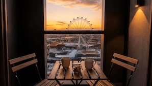 En balkon med et træbord og to stole, med udsigt over en by og et pariserhjul i solnedgang.