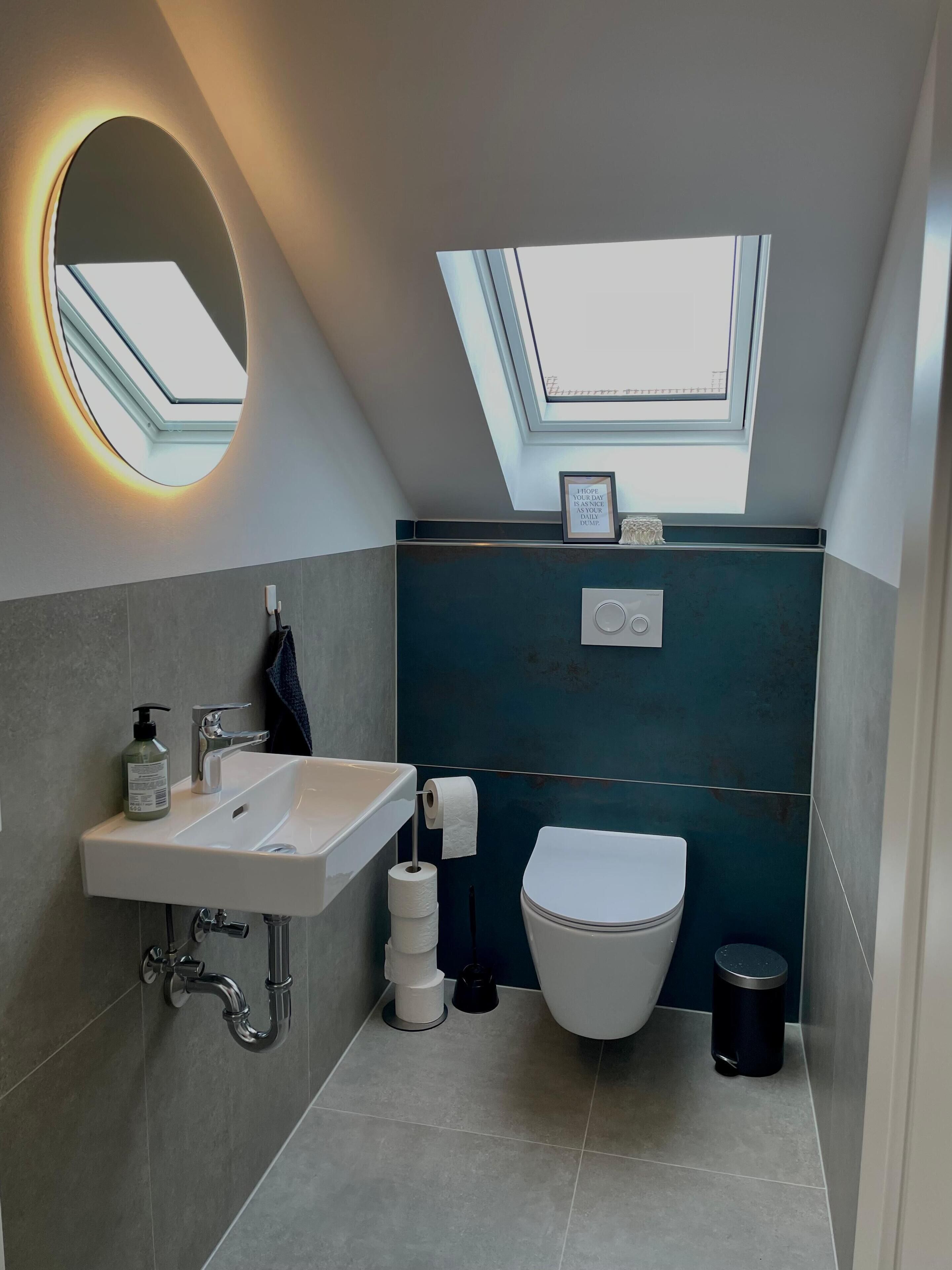 Un baño moderno con tragaluz, un lavamanos, un inodoro y un cubo de basura.