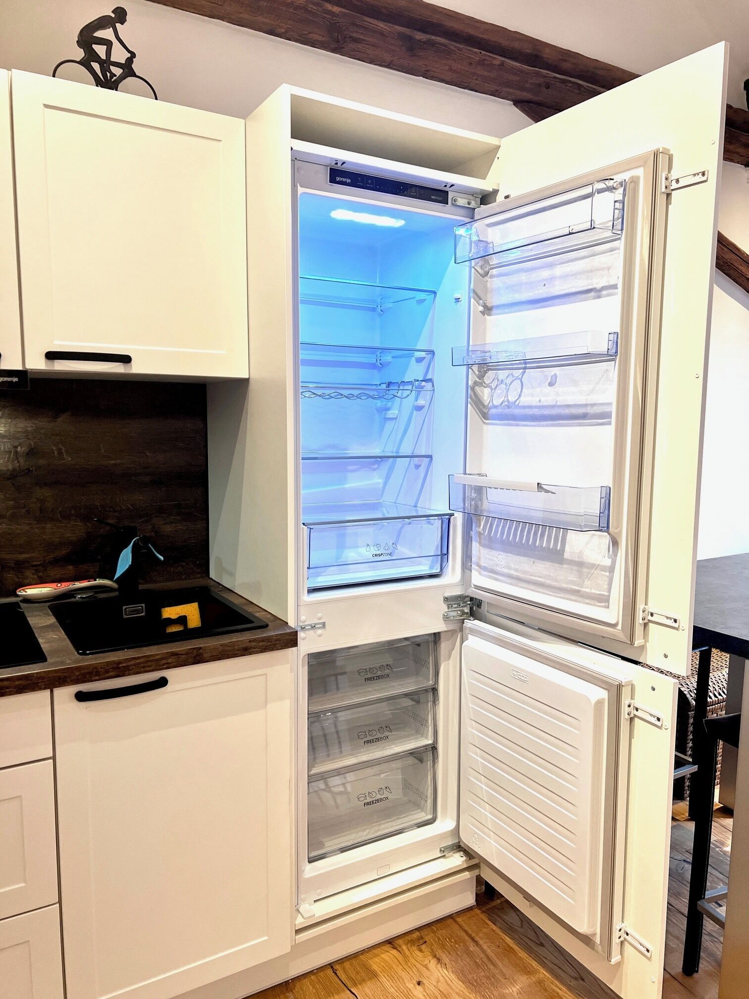 Une cuisine équipée d’un réfrigérateur encastré, d’un évier et de meubles de rangement en bois.