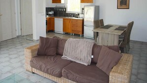 Una sala de estar con sofá, una mesa de comedor con sillas, una zona de cocina con armarios y electrodomésticos, y una puerta con espejo.
