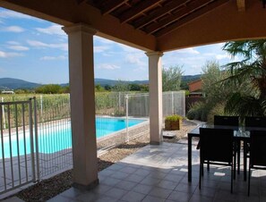 A covered outdoor area with a swimming pool, surrounded by a white fence, and a view of distant hills. - Blue Hills Residence With Scenic Views (Sampzon)