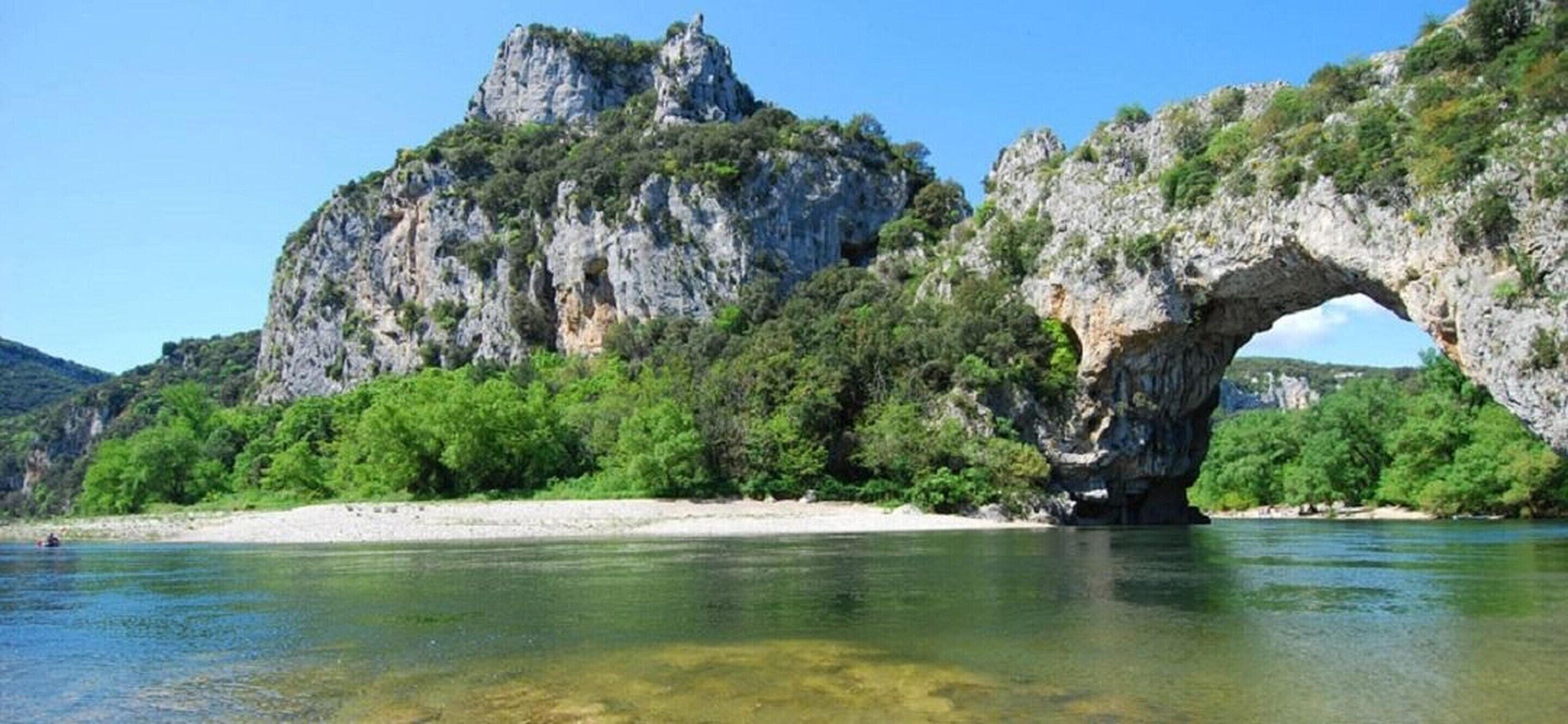 A natural landscape with a prominent rock formation and a large arch over a river.