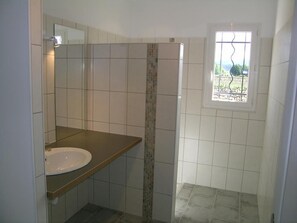 Een badkamer met een wit wastafelmeubel, een spiegel en een raam met uitzicht op groen.