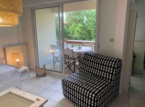 A room with a bed, a sofa, a table, and a chair. There is a sliding glass door leading to an outdoor area with a table and chairs. - Quiet T2 with garden & terrace - Hossegor center, 10 min plage / Beach (Soorts-Hossegor)