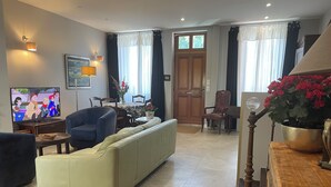 A living room with a sofa, chairs, a TV, a dining table, and a door.