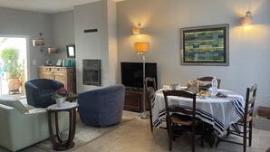 A dining area with a table set for two, a sofa, a television, and a fireplace.