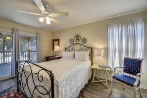A bedroom with a bed, a ceiling fan, a chair, a nightstand, and a window with curtains. - Big Views! Direct Beach Boardwalk Access! (St George Island)