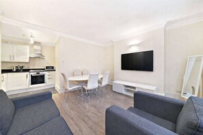 A modern living room with a dining area, a flat-screen TV mounted on the wall, and a kitchen with white cabinets and appliances. - New Oxford Street Central Apartment (London)