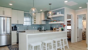 Een moderne keuken met witte kasten, een centraal eiland met barkrukken, roestvrijstalen apparatuur en een blauwe tegelachtergrond.