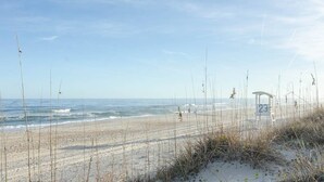 Een strand met een zandstrand, een houten constructie met het nummer 23, en schaarse begroeiing.