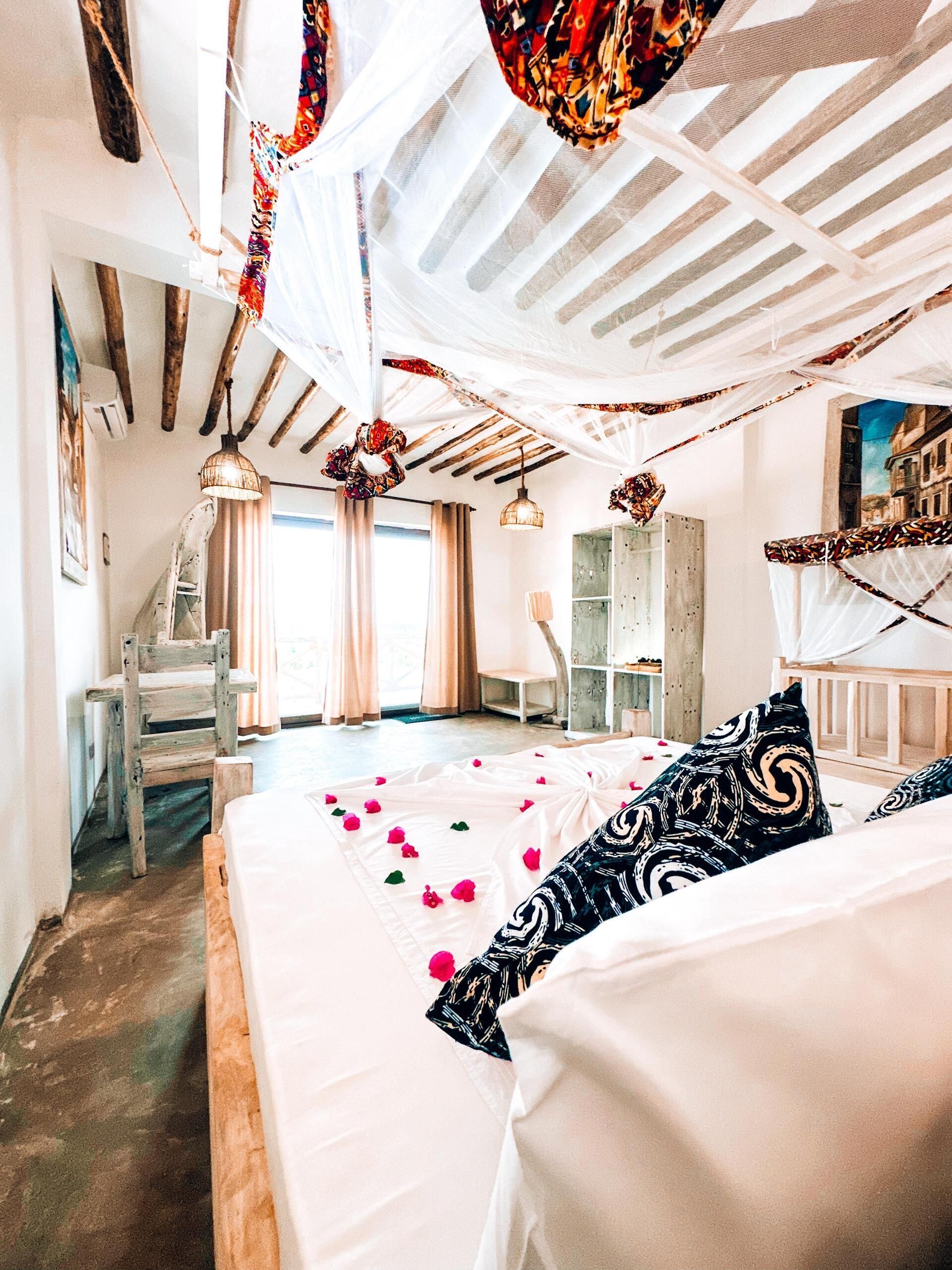 Une chambre à coucher avec un grand lit, une chaise en bois, un bureau et une vue sur l’extérieur par une fenêtre.