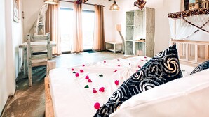 Ein Schlafzimmer mit einem großen Bett, einem Holzsessel, einem Schreibtisch und Blick ins Freie durch ein Fenster.