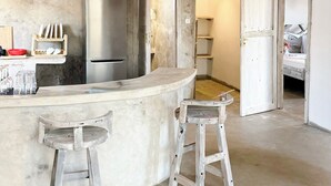 Eine Küche mit Marmorarbeitsplatte, zwei Barhocker, einem Kühlschrank und einer Holzbalkendecke.
