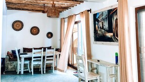 Ein rustikales Interieur mit freiliegenden Holzbalken, einem Deckenventilator, einem Essbereich mit Tisch und Stühlen sowie einem großen Gemälde an der Wand.