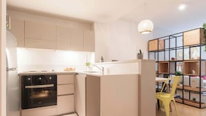Una cocina moderna con horno integrado, una zona de comedor con una silla amarilla y un espacio de sala de estar con sofá y una mesa de centro.