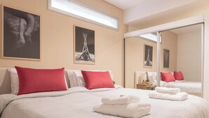 Una habitación de hotel con una cama grande, almohadas rojas, ropa de cama blanca y un espejo que refleja la habitación.