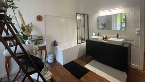 Un baño moderno con un espejo grande, dos lavamanos, una bañera y una silla de madera.