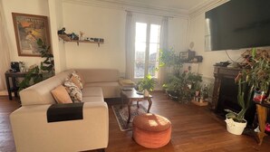 Una sala de estar con sofá, reposapiés, mesa de centro y varias plantas. Hay una chimenea y un televisor montado en la pared.