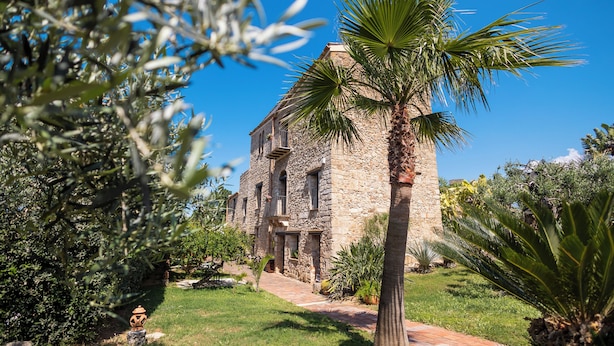 Un edificio de piedra con jardín y palmeras.