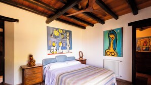 Un dormitorio con cama, mesitas de noche de madera, cómoda y dos cuadros en la pared.