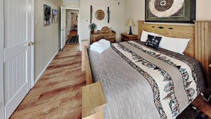 Ein Schlafzimmer mit Holzboden, einem Bett mit gemustertem Patchwork, einem Nachttisch, einer Lampe und einem Wandbild in Form eines Kreises.