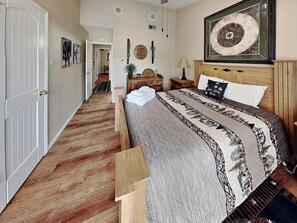Ein Schlafzimmer mit Holzboden, einem Bett mit gemustertem Patchwork, einem Nachttisch, einer Lampe und einem Wandbild in Form eines Kreises.