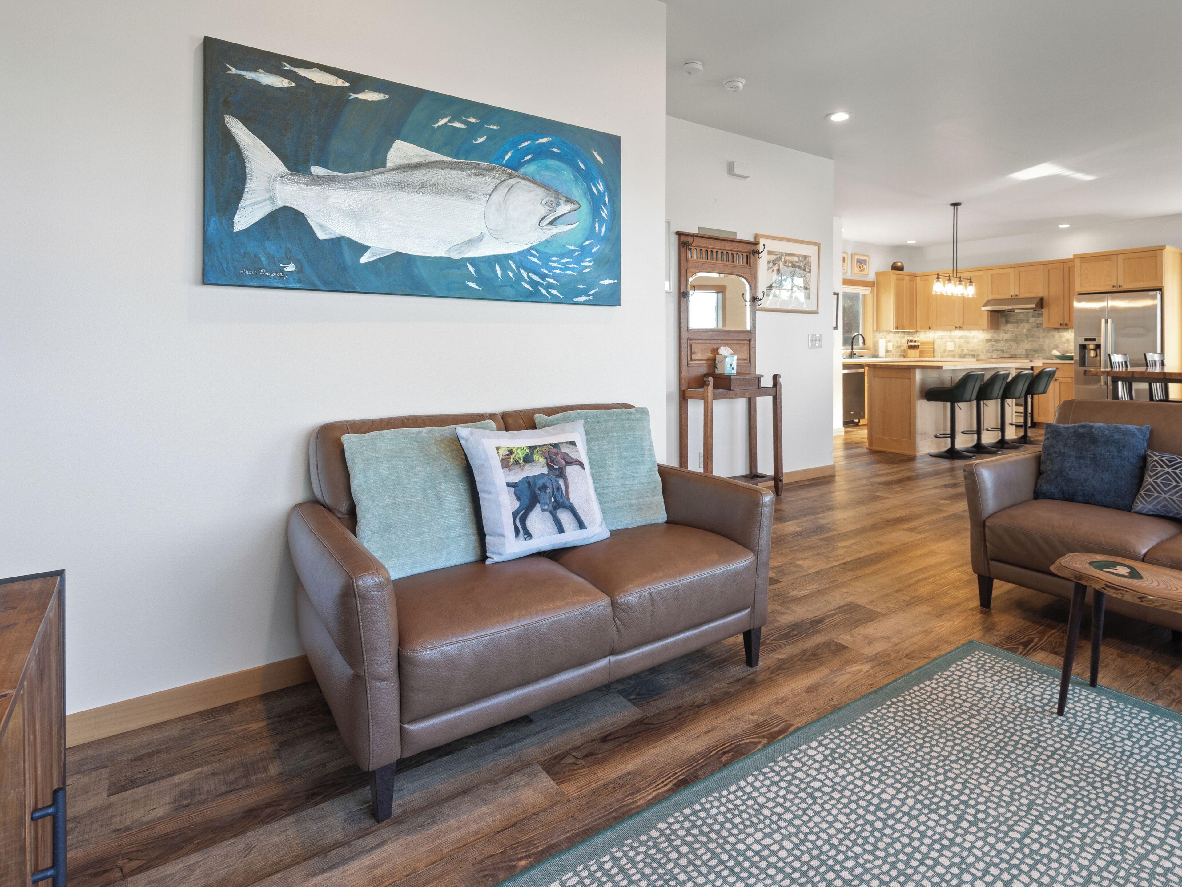 A modern living room with a brown leather sofa, a coffee table, and a painting of a fish on the wall.
