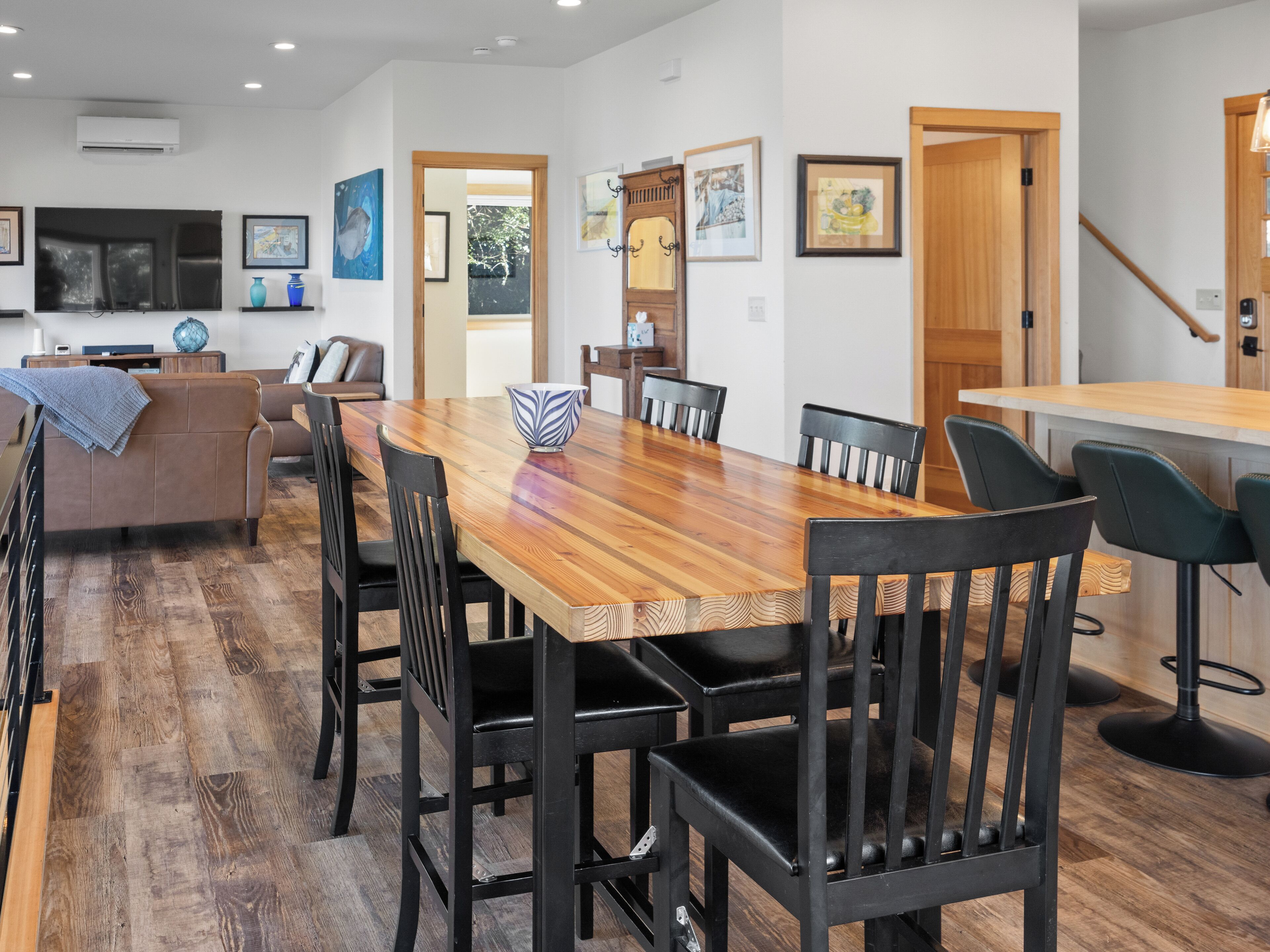 Un comedor moderno con una mesa de madera y sillas negras, una cocina al fondo y obras de arte en las paredes.