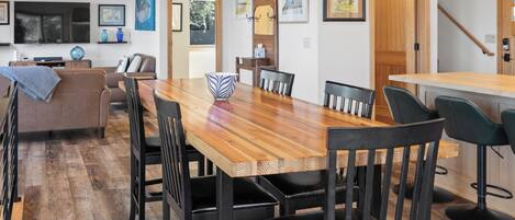 Un comedor moderno con una mesa de madera y sillas negras, una cocina al fondo y obras de arte en las paredes.