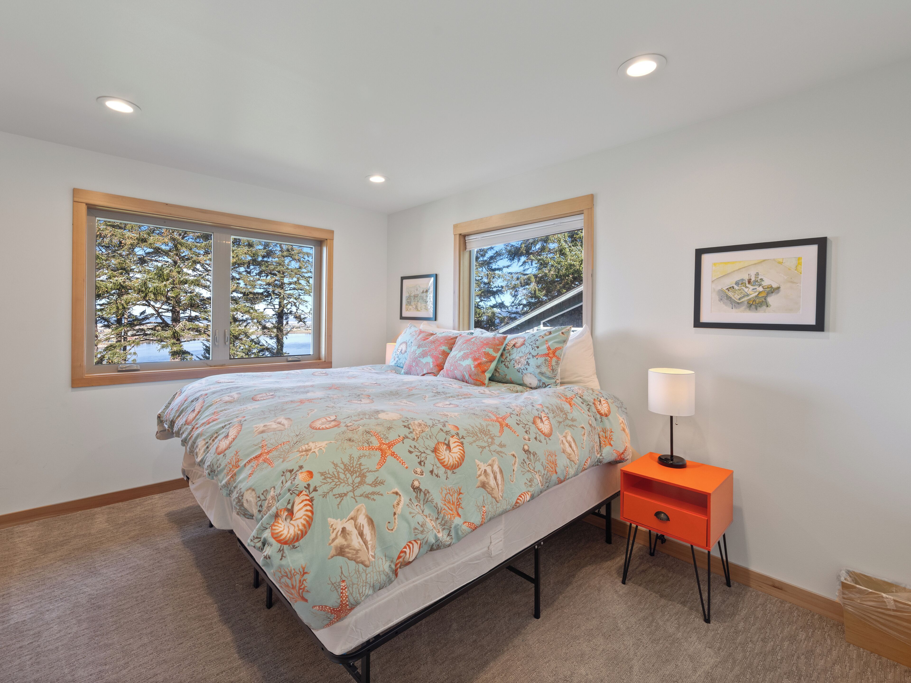 A bedroom with a bed, two windows, a nightstand, and a wall-mounted lamp.