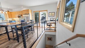 Een moderne keuken met houten kastjes, een roestvrijstalen koelkast en een eethoek met een zwarte metalen balustrade.