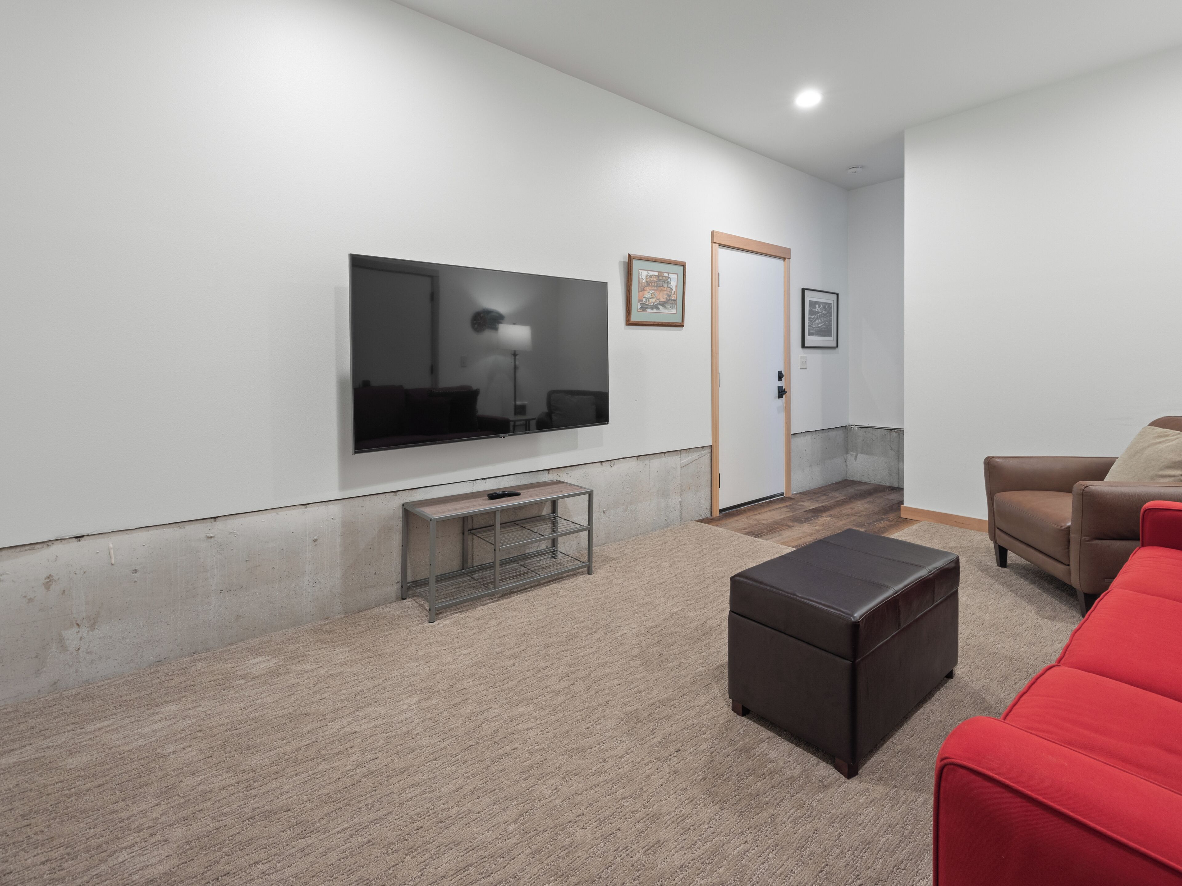 Een moderne woonkamer met een grote flatscreen televisie, een houten salontafel, een rode bank en een deur die naar een andere kamer leidt.