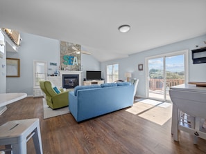 A spacious living area with a blue sofa, a green armchair, a fireplace, and a TV. - SunKissed Beach House | 2-Min Walk to Beach (Emerald Isle)